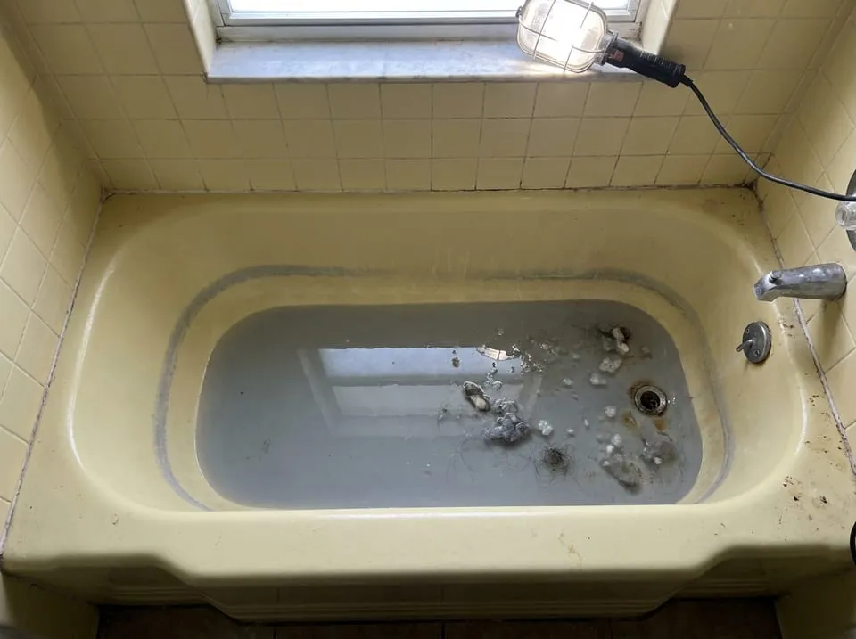 Gray lint-flecked water standing in an older Florida bathtub after a washing machine drain backup